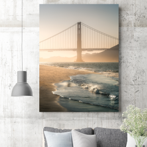 Photograph of the Golden Gate Bridge at sunset with waves lapping at the shore in San Francisco.